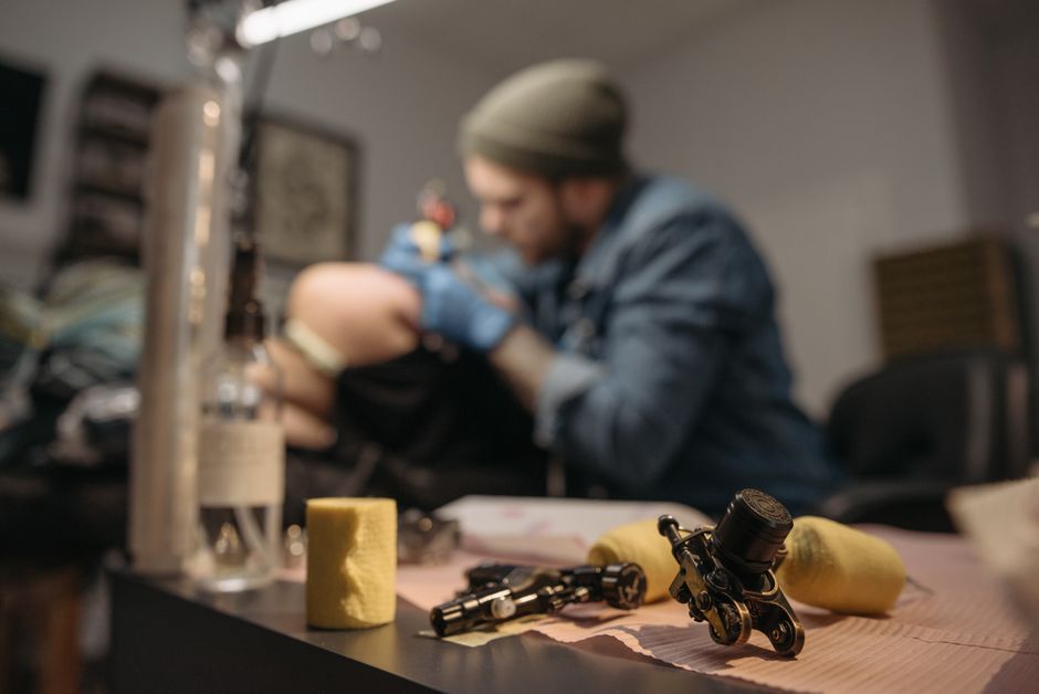 Tatuatore professionista che tiene in mano una pen machine moderna in uno studio di tatuaggi professionale illuminato.